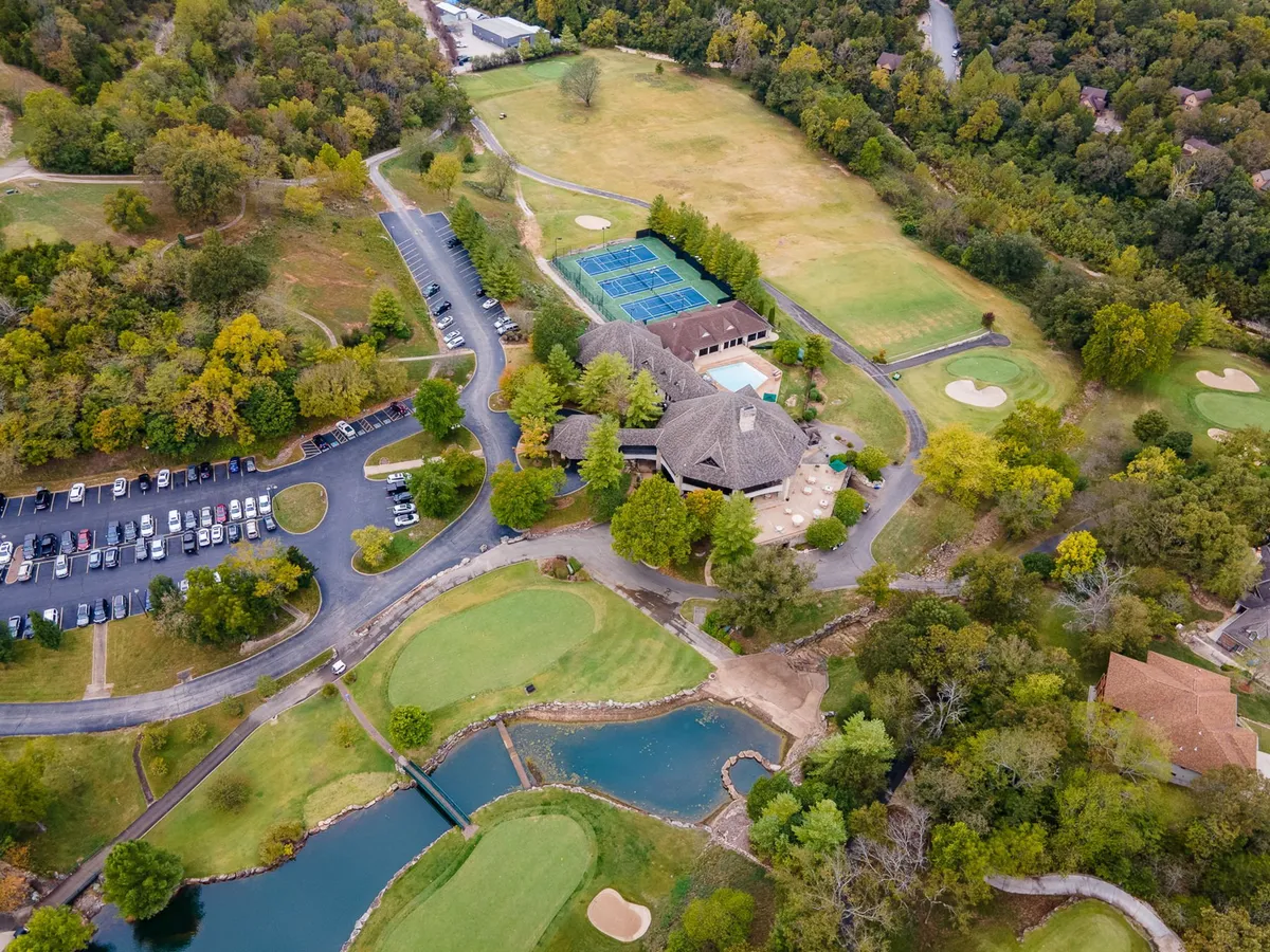 A panoramic exterior shot capturing the golf course, tennis courts, swimming pool, and clubhouse from above, with guests engaged in recreational activities and greenery all around.