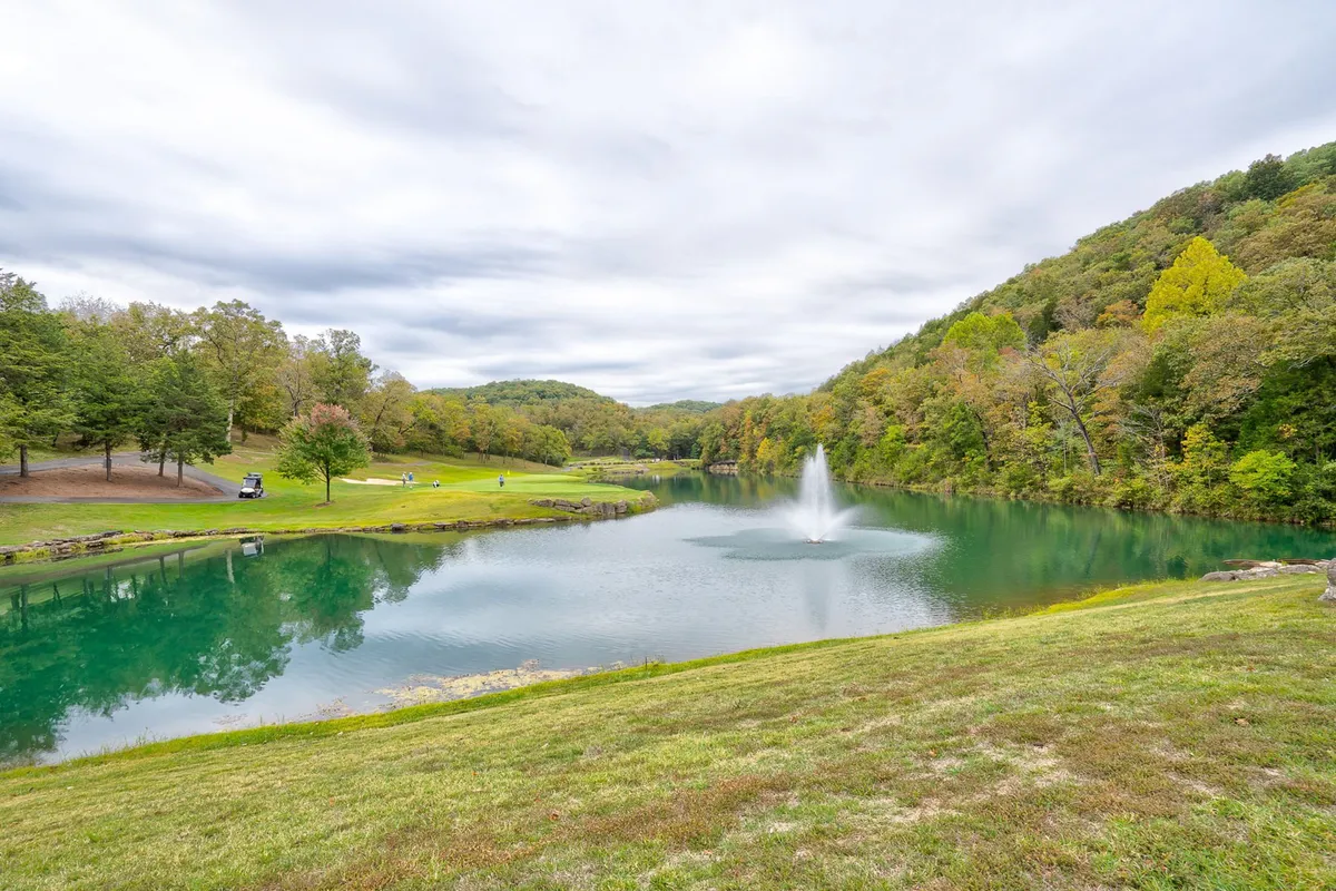 This serene view captures a large lake with a central fountain, bordered by trees and hills. The tranquil setting invites guests to enjoy fishing, leisurely walks, or simply taking in natural beauty, underlining the private, scenic aspects of the resort community.