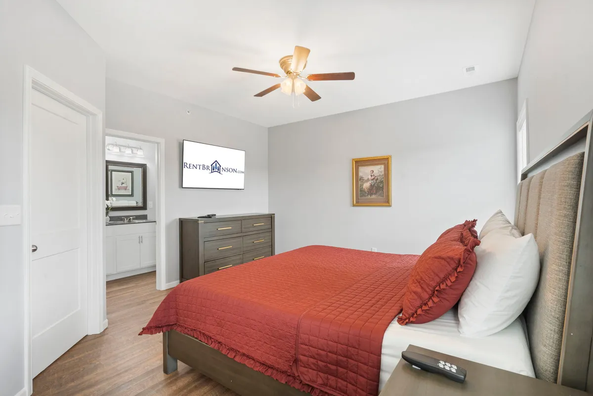 A cozy king bedroom featuring a plush bed with a red quilt, wall-mounted TV, dresser, framed artwork, and soft lighting. The room exudes comfort and a sense of privacy, ideal for unwinding after a day of adventure.