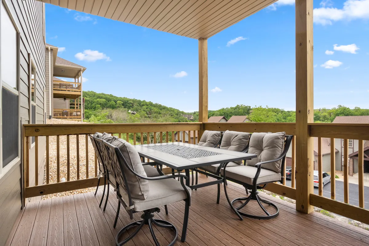 An inviting outdoor dining area set on a deck surrounded by lush greenery, with a scenic view stretching across gently rolling hills. The space features a table and chairs ready for al fresco meals with loved ones, bathed in warm natural light, ideal for both sunrise coffees and sunset gatherings.