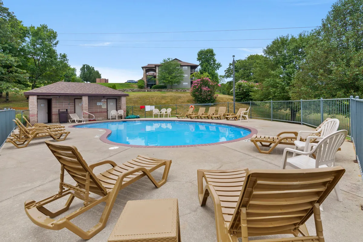This image showcases a sparkling outdoor swimming pool surrounded by lounge chairs and shaded by trees, with a poolside gazebo visible nearby. The inviting water and ample seating establish a vibrant, resort-like environment perfect for relaxing, sunbathing, or socializing.
