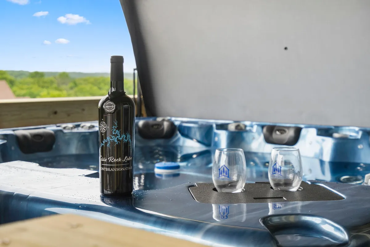 A cozy hot tub set beside a table with a wine bottle and glasses, creating a tranquil, intimate atmosphere. Large windows or an open view suggest a connection between the comfort of the hot tub experience and the natural surroundings, ideal for relaxing after a day of activities.