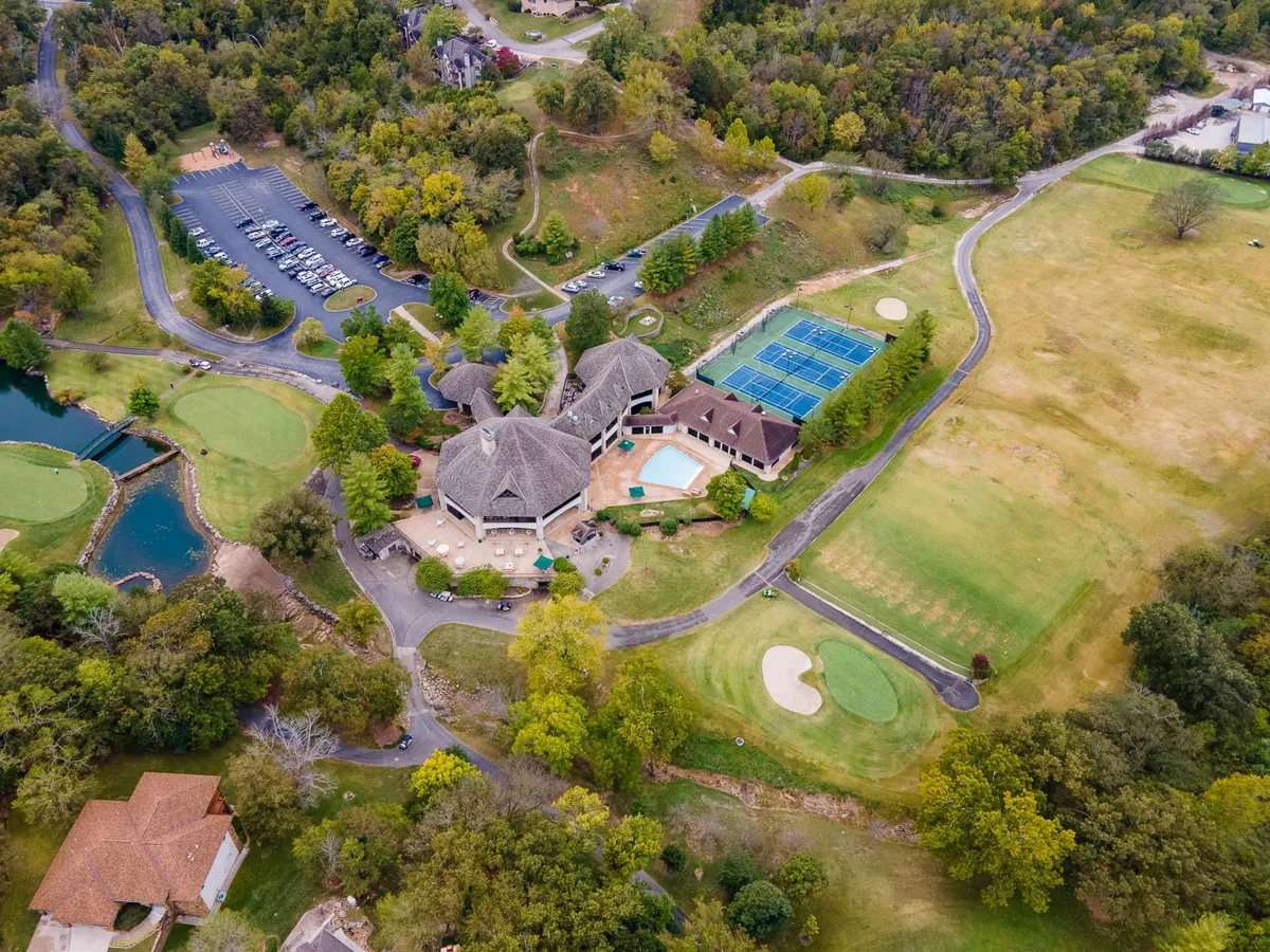 A wide-angle exterior shot showcasing a vibrant golf course, sparkling swimming pool, inviting tennis courts, and the elegant clubhouse, all set beneath a picturesque sunset. Small groups of people are seen golfing, swimming, and socializing, highlighting the lively, resort-style atmosphere.