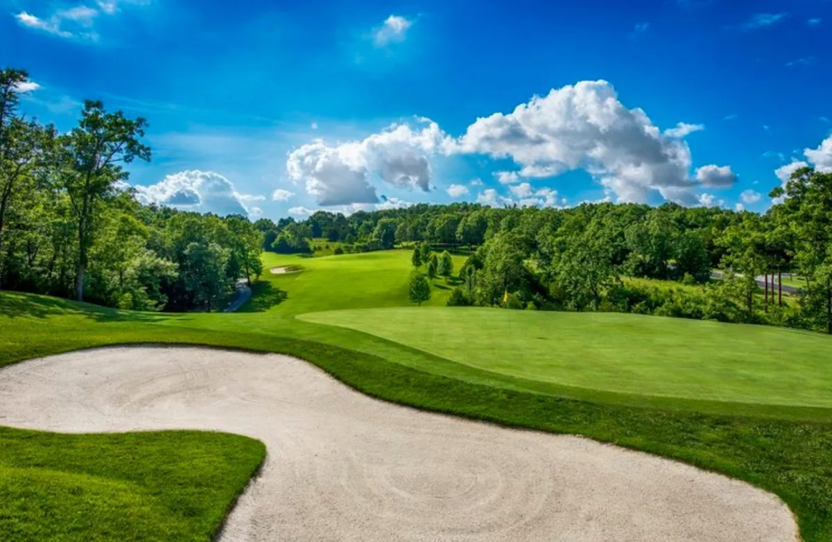 This image shows the lush greens of a golf course, including a sand trap and a wide expanse of sky with scattered clouds. The course is well-maintained and inviting, set against a serene natural backdrop.