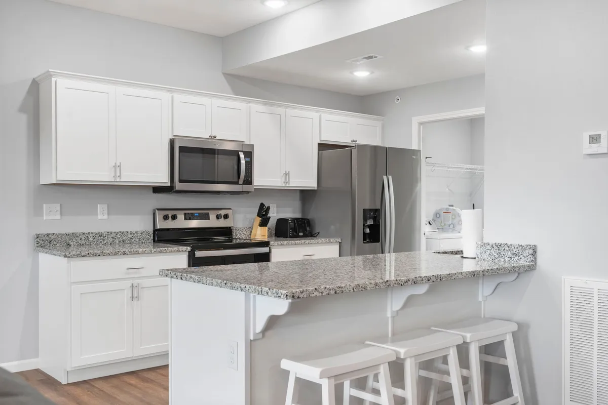 A modern kitchen space featuring granite countertops, stainless steel appliances, white cabinetry, and bar stools, designed for cooking, entertaining, and casual family meals.