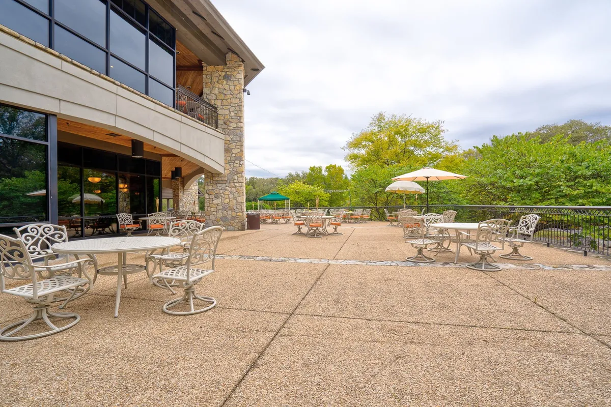 A serene outdoor seating area with umbrella-covered tables surrounded by lush greenery. The setting encourages leisurely meals, socializing, and enjoying the fresh air, ideal for families or groups looking to relax together.